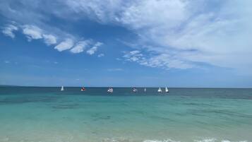 A beach with clear turquoise waters and a row of sailboats.