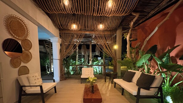 A cozy outdoor seating area with wicker furniture, a central wooden coffee table, and a decorative wall with woven patterns. - Hotel Casa Bajari (Pedernales)