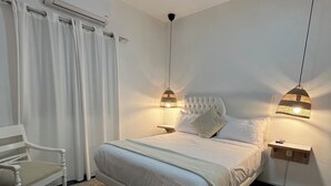 A bedroom with a bed, two bedside tables, a chair, an air conditioning unit, and a hanging light fixture. - Hotel Casa Bajari (Pedernales)