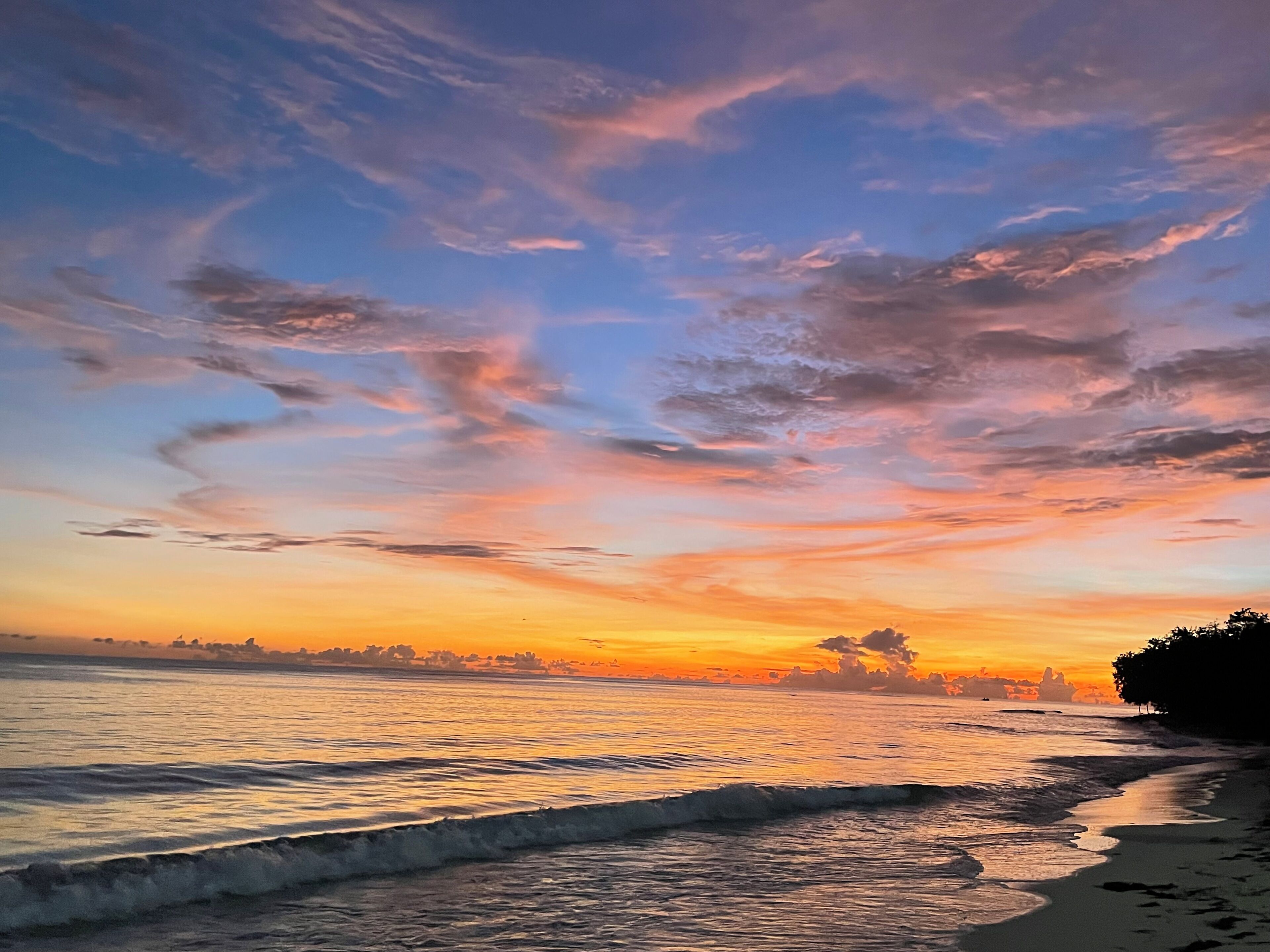 Una playa con olas al atardecer, cielo despejado y tierra a lo lejos.