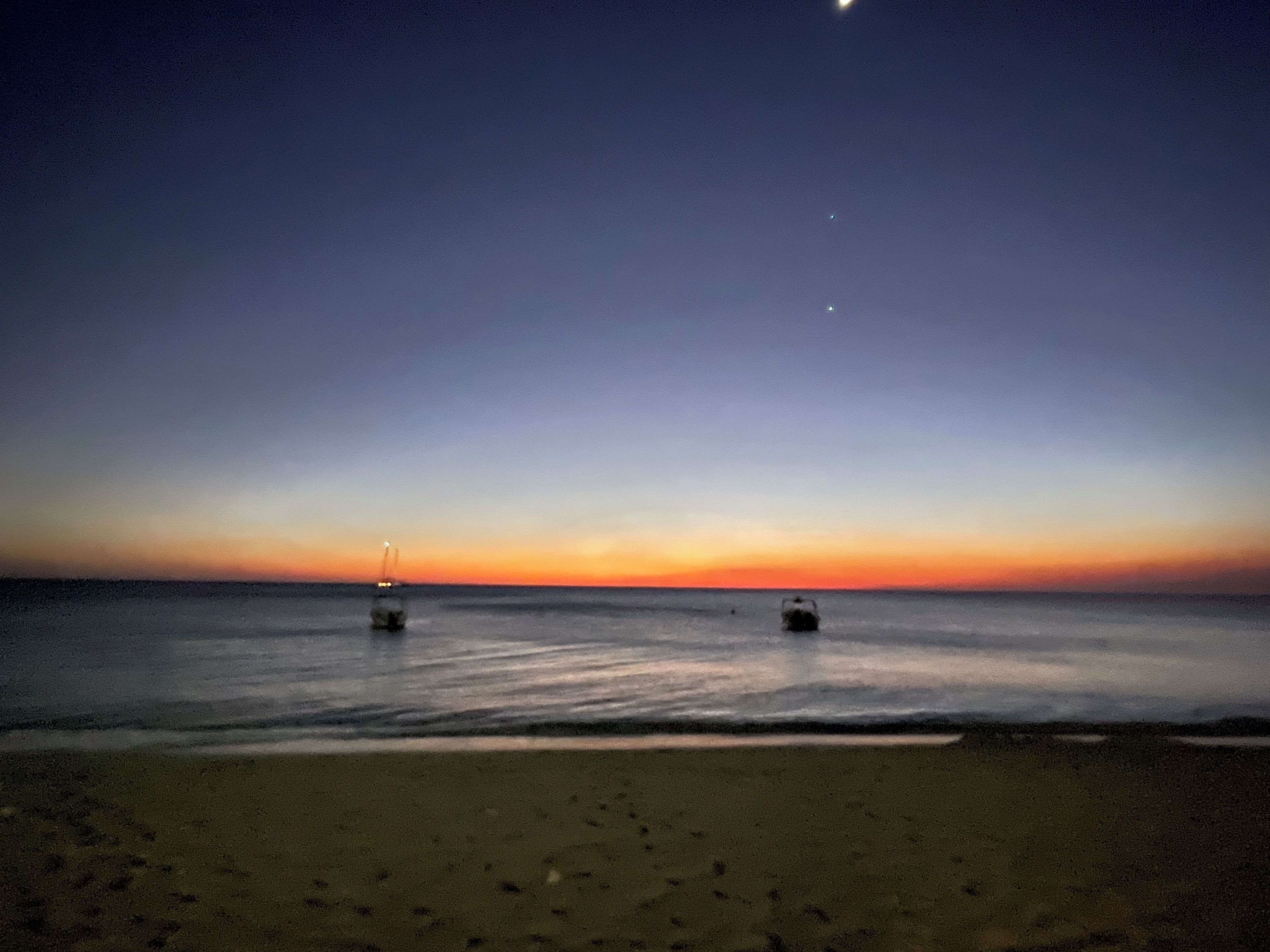 A beach at sunset with calm waters and a clear sky.