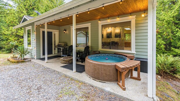 A covered outdoor area with a hot tub, seating, and a grill.