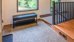 A spacious room with a large window, a wooden bench, and a staircase.