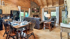 A wooden cabin interior with a dining area, a fireplace, a sofa, and a TV.