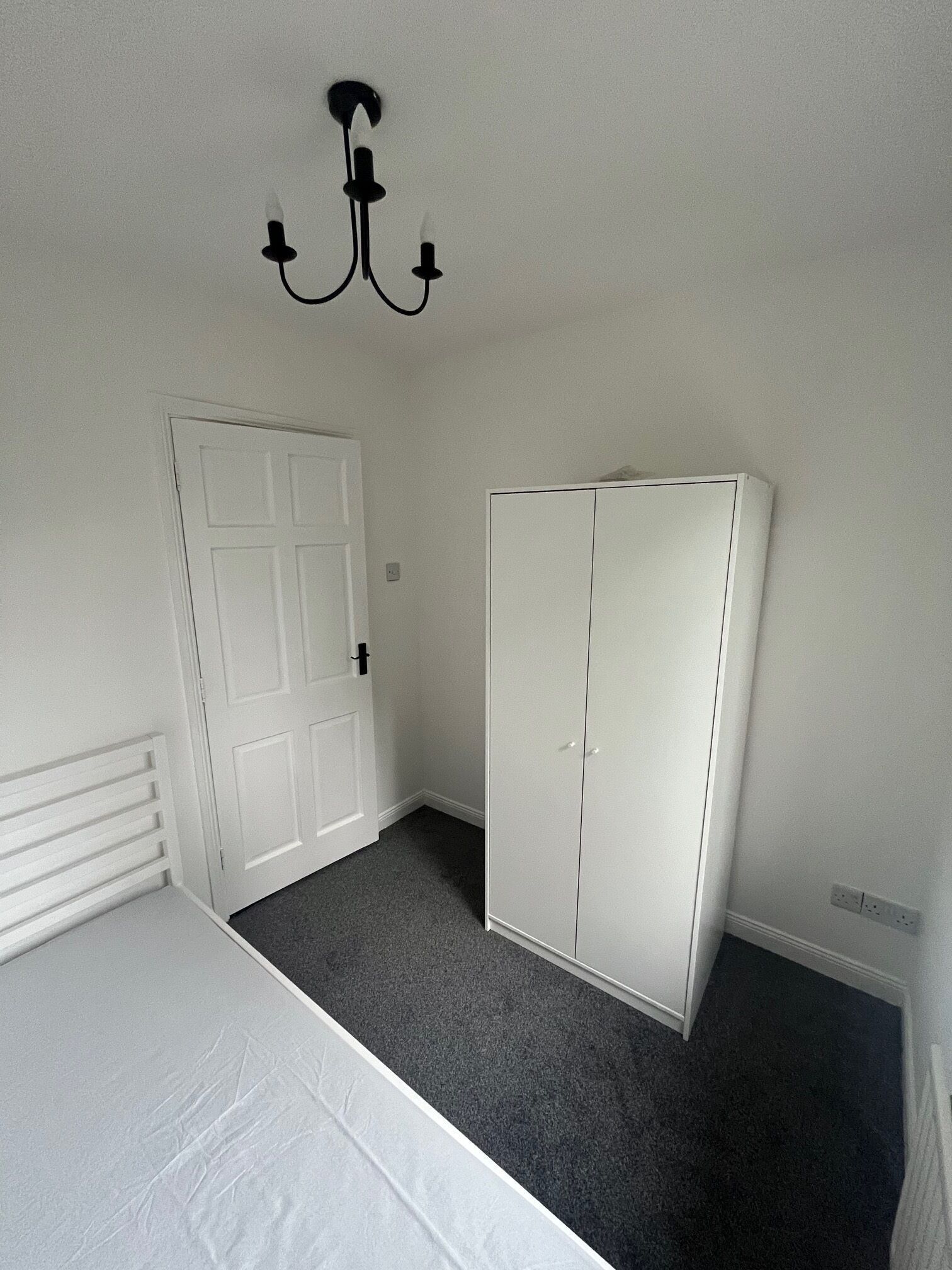 A room with a white door, a white wardrobe, and a white bed.
