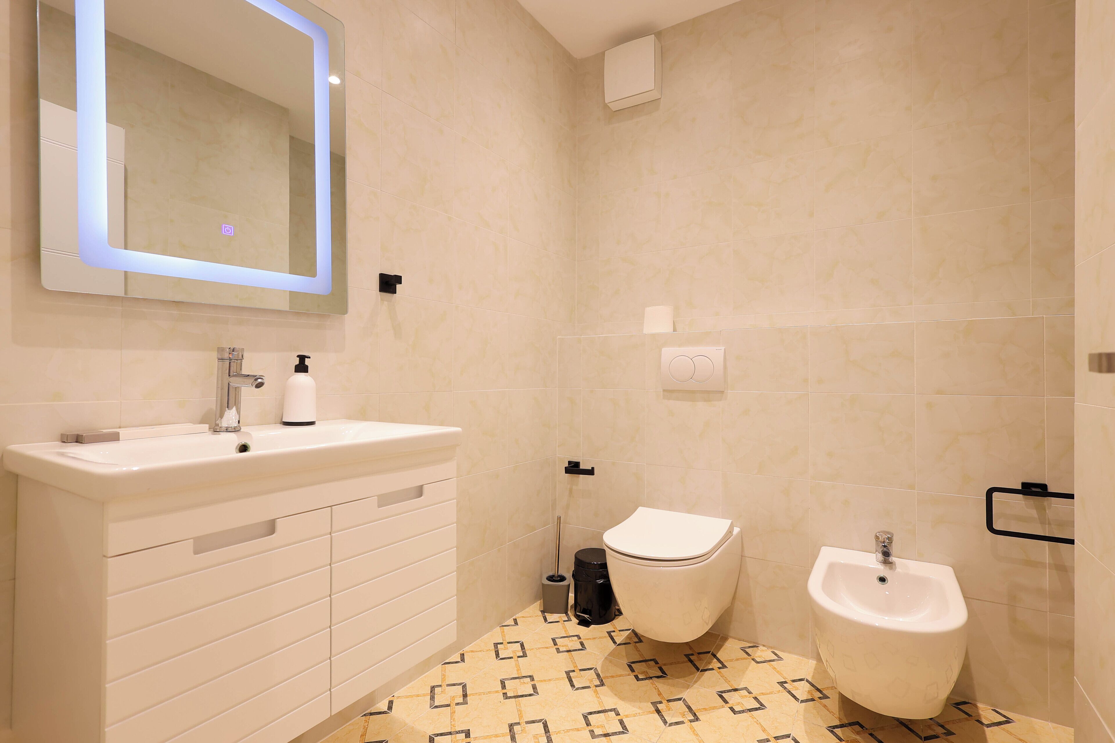 Une salle de bain moderne équipée d’un meuble-lavabo, de toilettes, d’un bidet et d’un miroir avec éclairage.