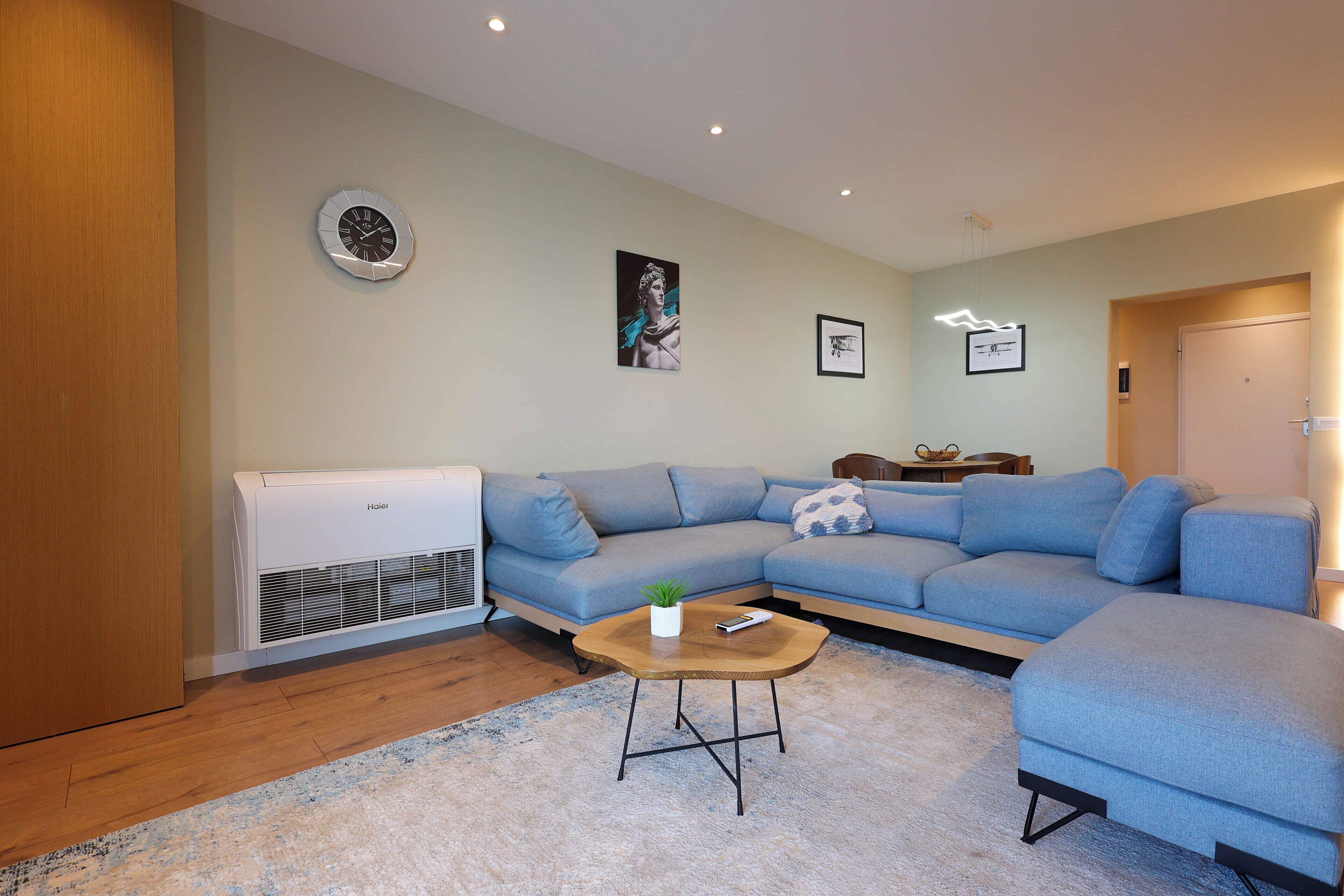 Un salon moderne avec un canapé d’angle, une petite table basse et un climatiseur fixé au mur.