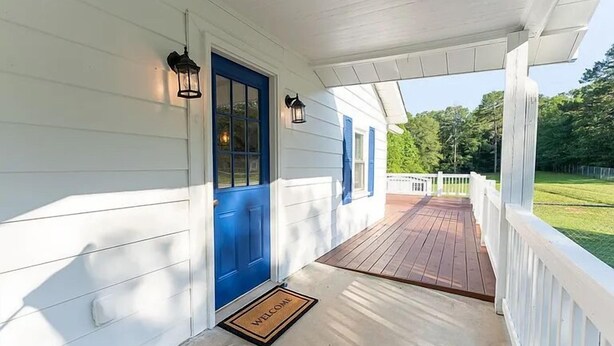 Un porche abrité avec une porte bleue, un paillasson et une terrasse en bois.
