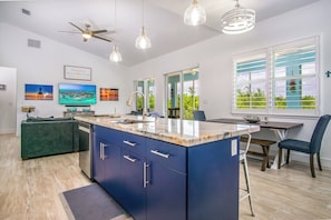 A modern kitchen with a large island, a dining area, and a living room with a sofa.