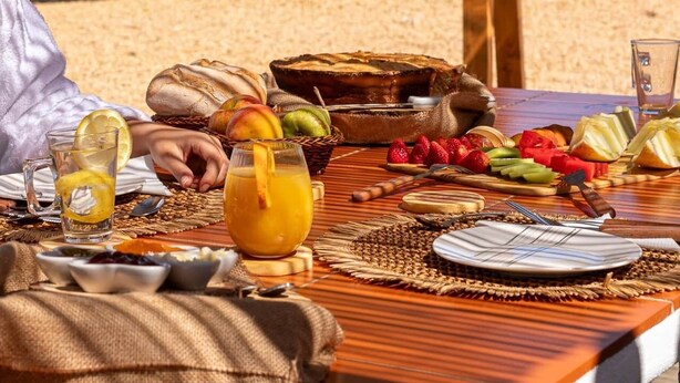 A wooden dining table set outdoors with various fruits, a jug of juice, and a picnic setup. - Monte dos Mestres (São Domingos)