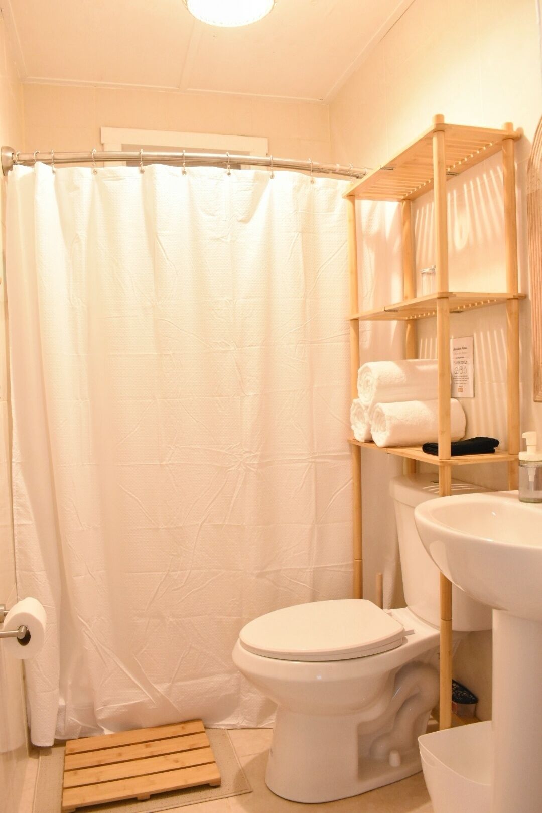 A bathroom with a toilet, a sink, a shelf with towels, and a shower curtain.