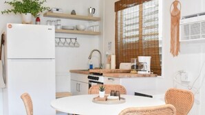 Een moderne keuken met een ronde eettafel, rieten stoelen, een witte koelkast en een houten plafond.