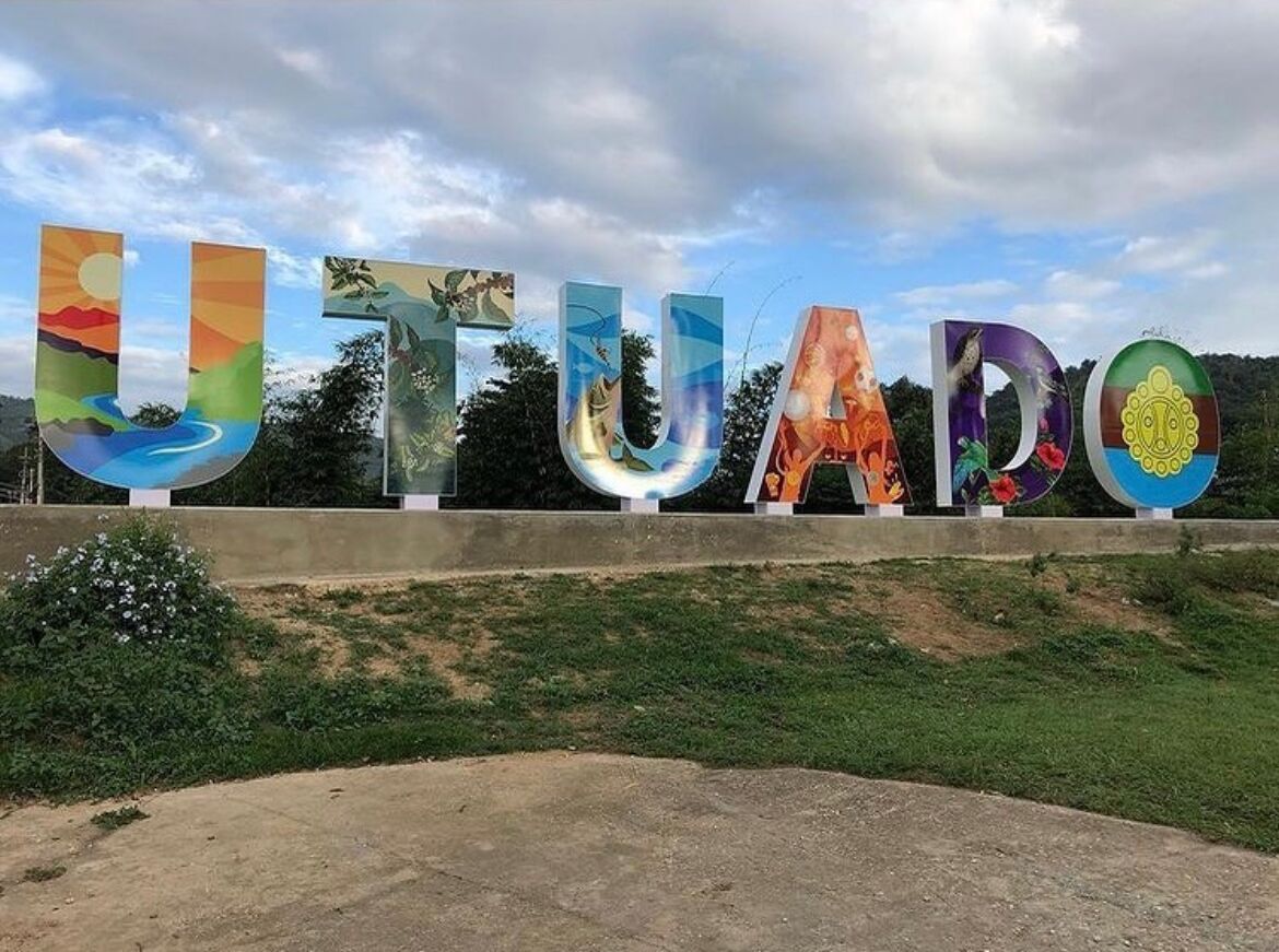 De grandes lettres colorées épellent le mot « UTUADO » sur un fond représentant un paysage pittoresque.