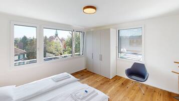 Ein modernes Hotelzimmer mit einem großen Bett, einem Schreibtisch und zwei Fenstern mit Blick auf die Stadt.