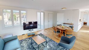 A spacious living area with a flat-screen TV, a dining table with chairs, and a sofa.