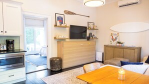 Une cuisine moderne équipée d’un four à micro-ondes, d’une machine à café et de meubles de rangement en bois. On y trouve également un coin repas avec une table et des chaises, ainsi qu’un petit tapis sur le sol.