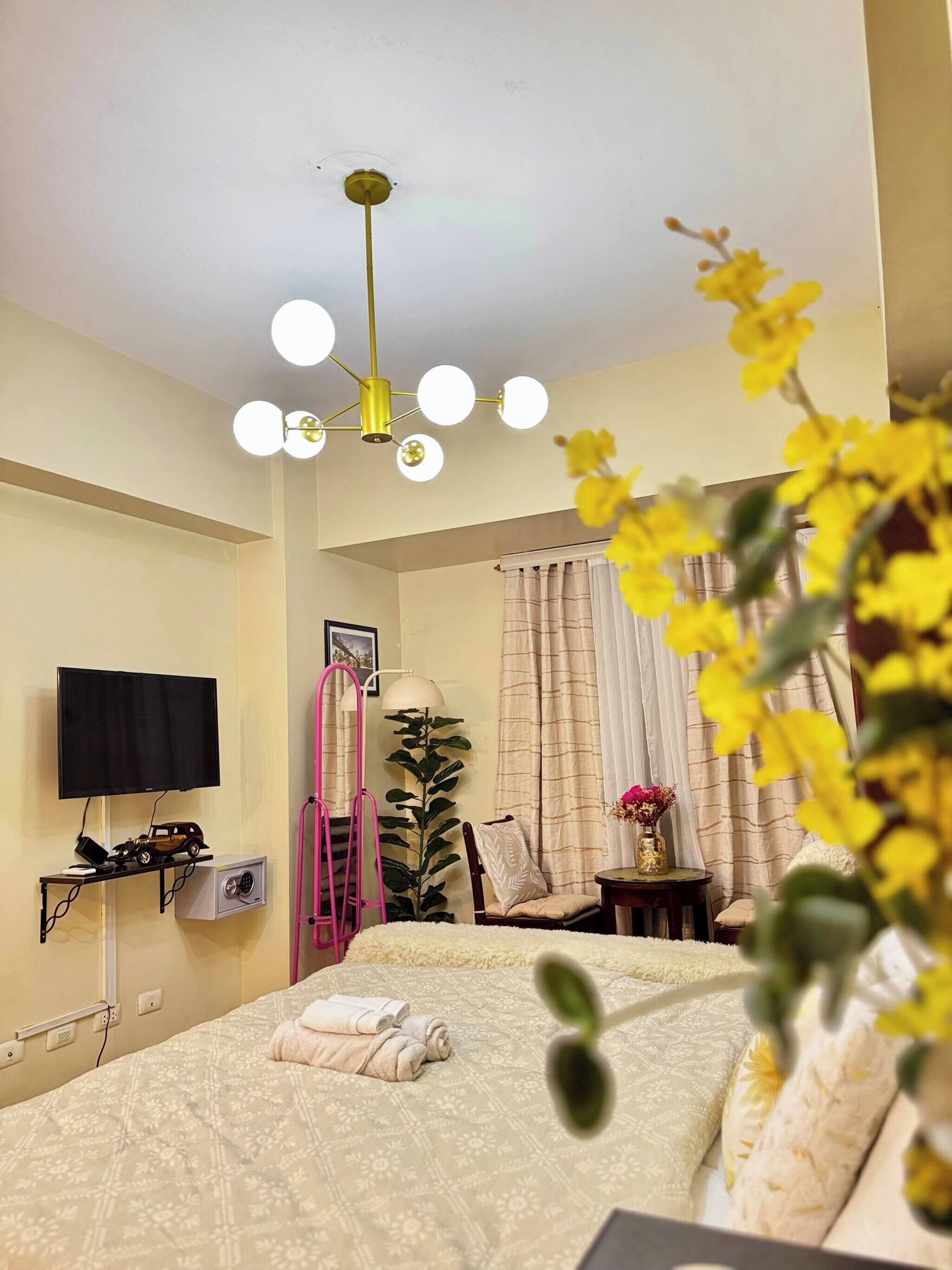 Una habitación de hotel con cama, televisión, escritorio, planta y lámpara en el techo.