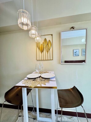 Een eetgedeelte met een witte tafel gedekt voor twee personen, een kroonluchter en een wandspiegel.