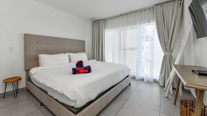 A hotel room with a large bed, a small table, a TV, and a window with curtains.