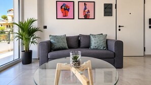 A modern living room with a grey sofa, two framed artworks, a potted plant, and a glass coffee table with a decorative item.