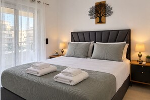 A neatly made bed with a grey quilt, two pillows, and two folded towels.