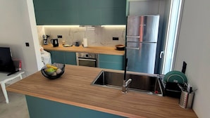 A modern kitchen with teal cabinets, a wooden countertop, and stainless steel appliances. - Jacuzzi Penthouse at Gazi nights (Athina)