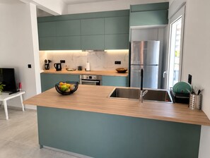 A modern kitchen with teal cabinetry, a stainless steel refrigerator, and a wooden island with a sink.