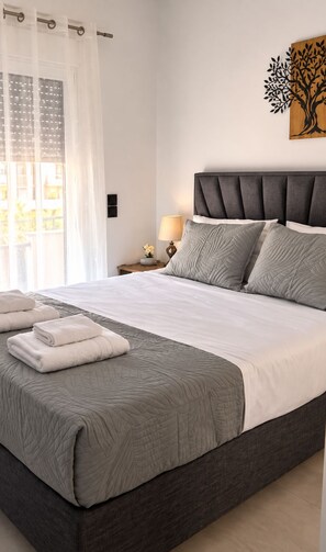 A neatly made bed with a grey quilt, white linens, and two folded towels.