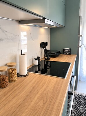 A modern kitchen with a black induction cooktop, wooden countertop, and a stainless steel range hood. There are jars of almonds and a paper towel holder on the counter.