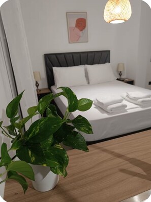 Ein Hotelzimmer mit Bett, Nachttischen, einer Topfpflanze und einem an der Wand befestigten Kunstwerk.