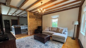Un salon spacieux avec des poutres apparentes, un grand canapé, une table basse et un tapis à motifs.