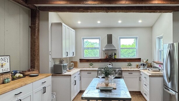 Une cuisine moderne avec des meubles blancs, un plafond en bois et un îlot central agrémenté d’un vase et de verres à vin.