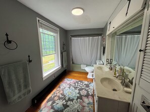 Ein Badezimmer mit großem Fenster, Duschvorhang, Toilette, Waschbecken und Spiegel.