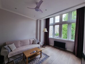A living room with a sofa, a coffee table, a floor lamp, and a window with curtains. - Renovated Spacious Bright by Regent's Park (London)
