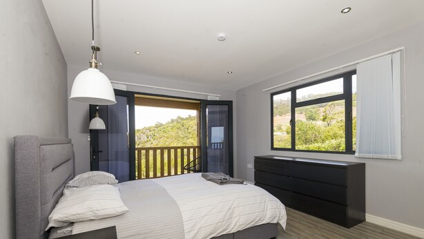 Un dormitorio con cama, cómoda, lámpara colgante y ventana con vista a follaje.