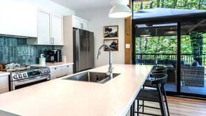 Een moderne keuken met een groot eiland, roestvrijstalen apparatuur en uitzicht op een terras met zitplaatsen.