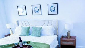 Una cama bien hecha con un plaid verde, una bandeja con una botella y vasos, y un reloj en la mesita de noche.