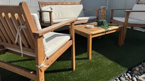 Un área de estar exterior de madera con una mesa, sillas y una planta pequeña.