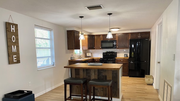 A modern kitchen with wooden cabinetry, a central island, and a black refrigerator. - Family Getaway Near Beaches, Sleeps 8 (New Port Richey)