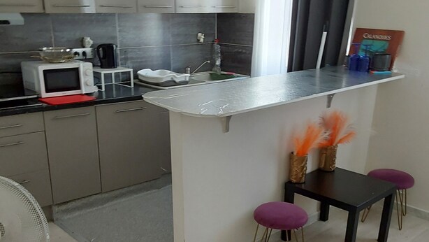 A compact kitchen with a microwave, kettle, and small sink. There is a dining area with a table and two purple stools. - T2 in the sun (Marseille)