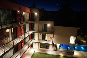 Un immeuble à plusieurs étages doté de balcons, d’une piscine et d’un éclairage extérieur soigné la nuit.