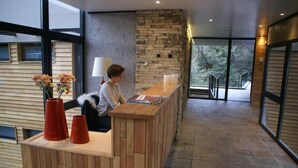 Un mostrador de recepción con detalles de madera, una pared de piedra y vistas a árboles a través de amplios ventanales.