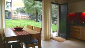 Un comedor con una mesa y sillas, vista a un patio trasero con césped y árboles, y una cocina con armarios y encimera.