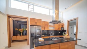 Una cocina moderna con armarios de madera, una isla central, electrodomésticos de acero inoxidable y un amplio ventanal que proporciona luz natural.