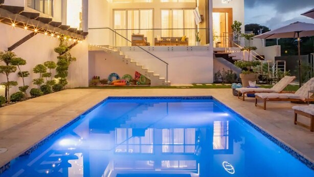 Una casa moderna con piscina, una escalera que lleva a un balcón y mobiliario exterior.