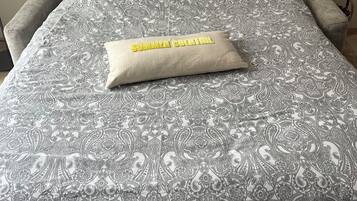 A bed with a patterned bedspread and a pillow labeled "SUMMER COCOA TIME".