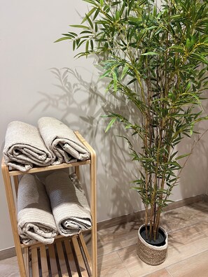 A wooden shelf with neatly folded towels and a potted bamboo plant. - Apartment in the heart of the city, close to historic sites, ideal for families (Verdun)