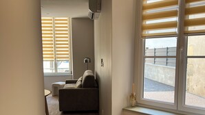 A modern living room with a sofa, a table, and a window with blinds. - Apartment in the heart of the city, close to historic sites, ideal for families (Verdun)