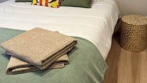 A neatly made bed with a green and white bedspread, two pillows, one with a lemon pattern, and a folded beige towel on the bed. - Apartment in the heart of the city, close to historic sites, ideal for families (Verdun)