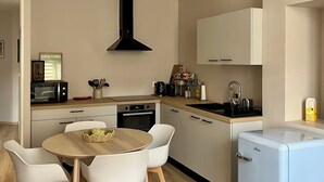 A modern kitchen with white cabinets, a black range hood, a microwave, and a small refrigerator. - Apartment in the heart of the city, close to historic sites, ideal for families (Verdun)